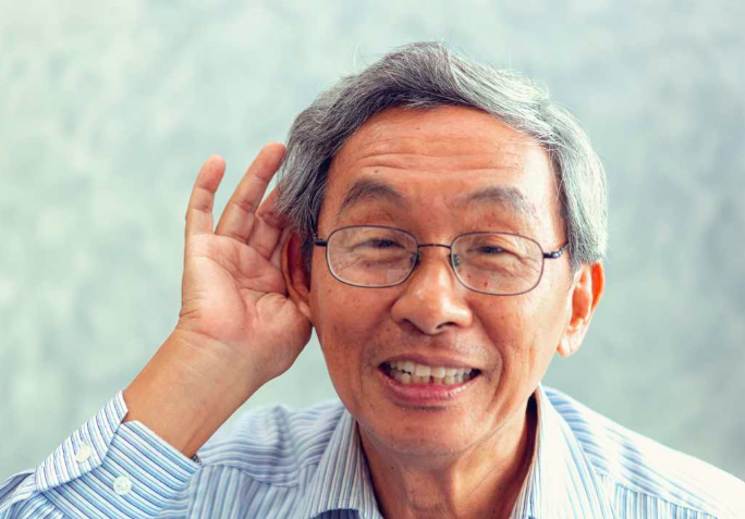 Elderly man with a hand up to his ear listening 