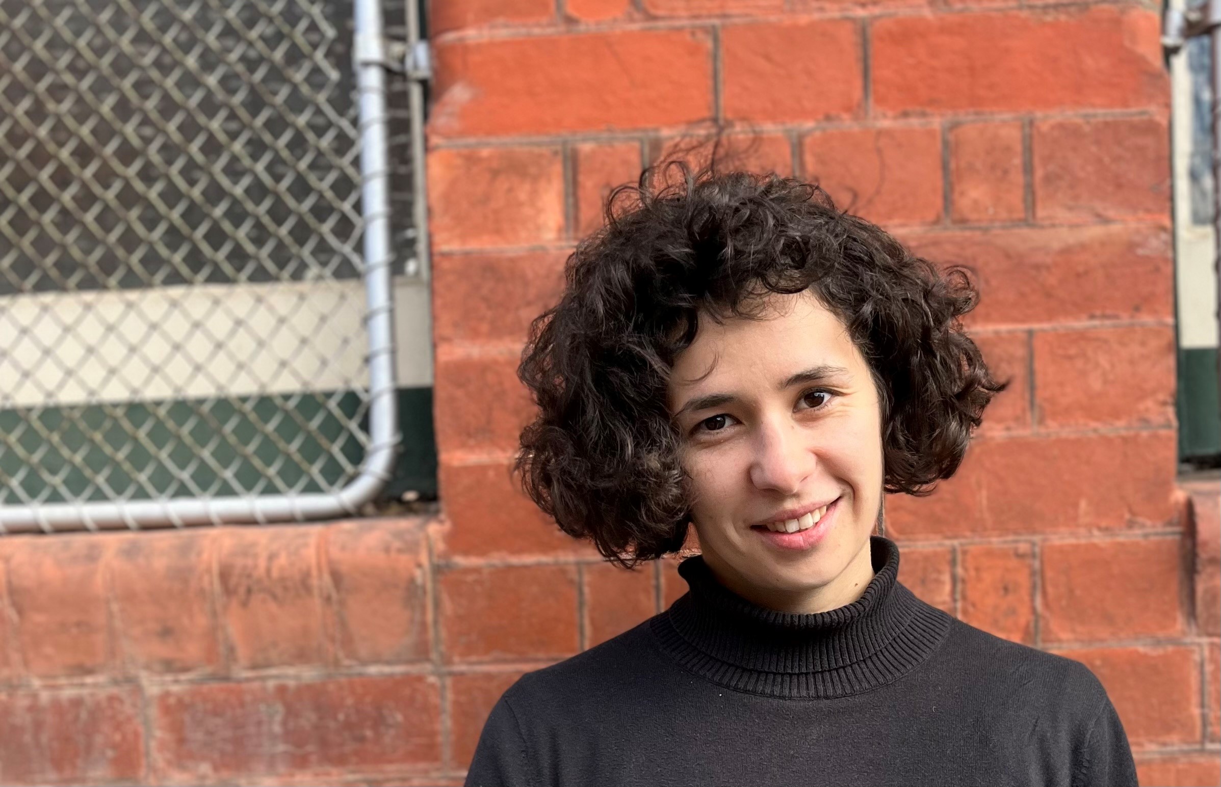 Dr Lucy Benjamin standing in front of a brick wall, smiling.