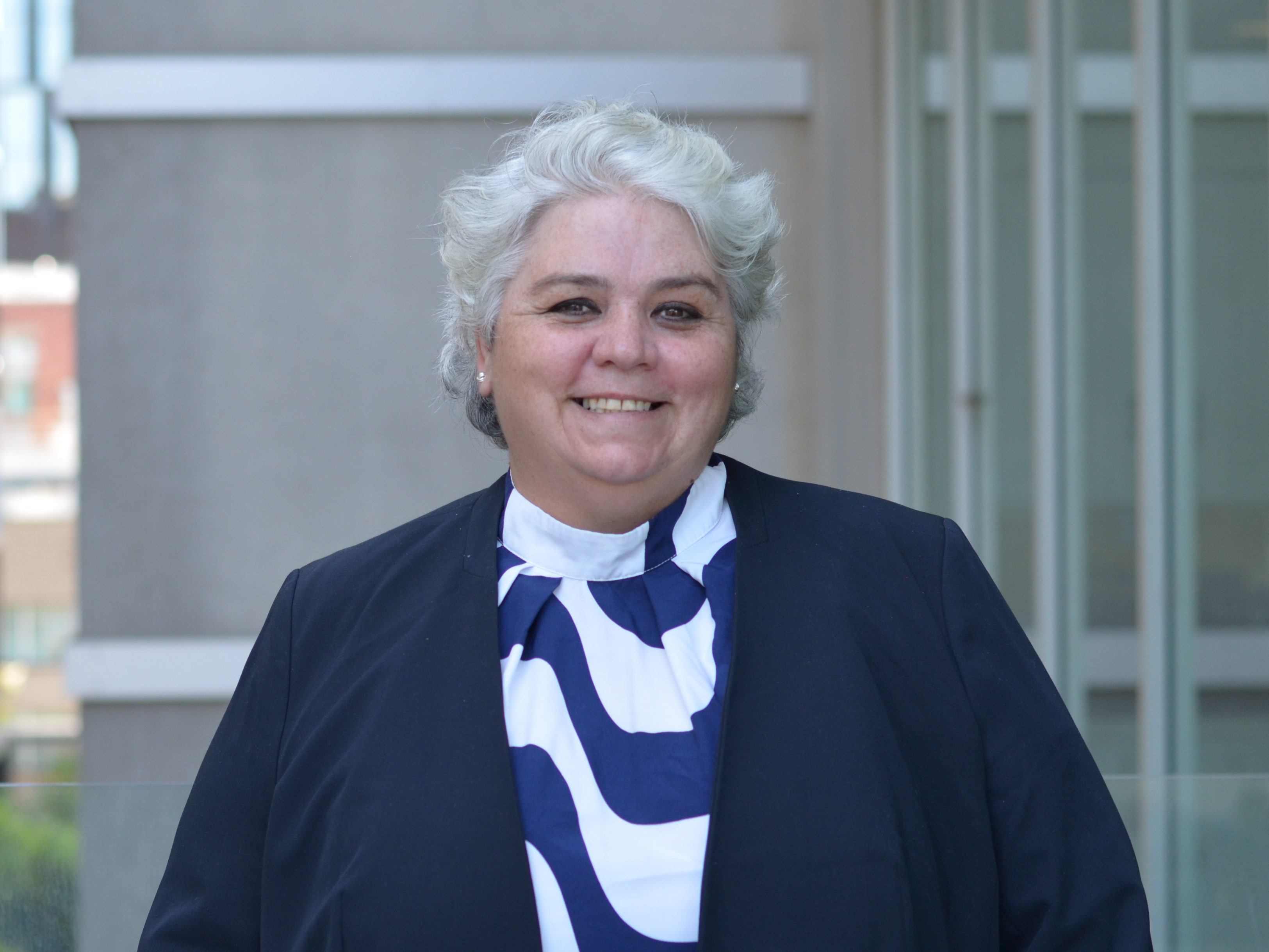 Professor Melitta Hogarth in a white and blue shirt, smiling outside the Faculty of Education.