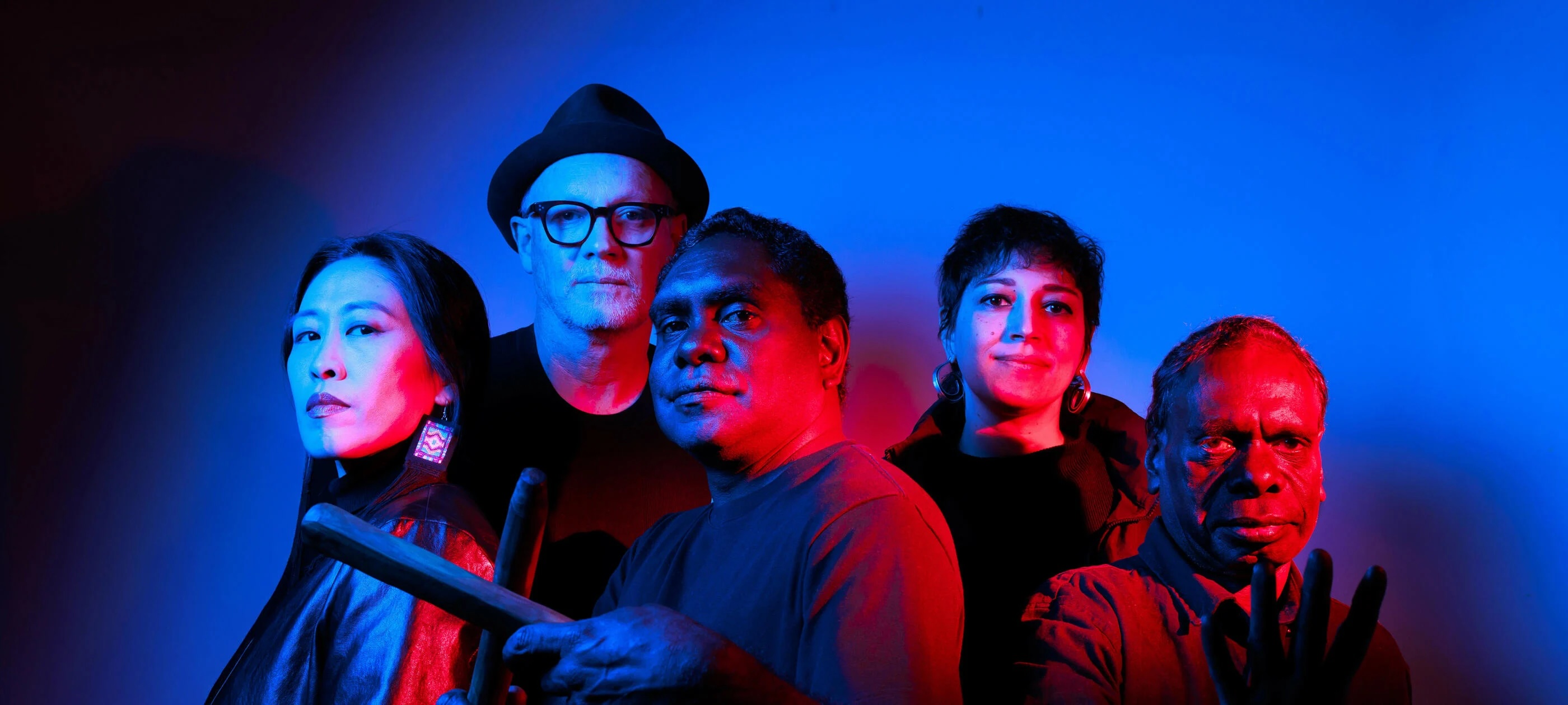 Five people stand in a line, one holding a traditional First Nations musical instrument
