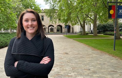 Portrait of Dr Chelsea Hyde standing in front of the South Lawn, with trees and the clocktower in the background. 