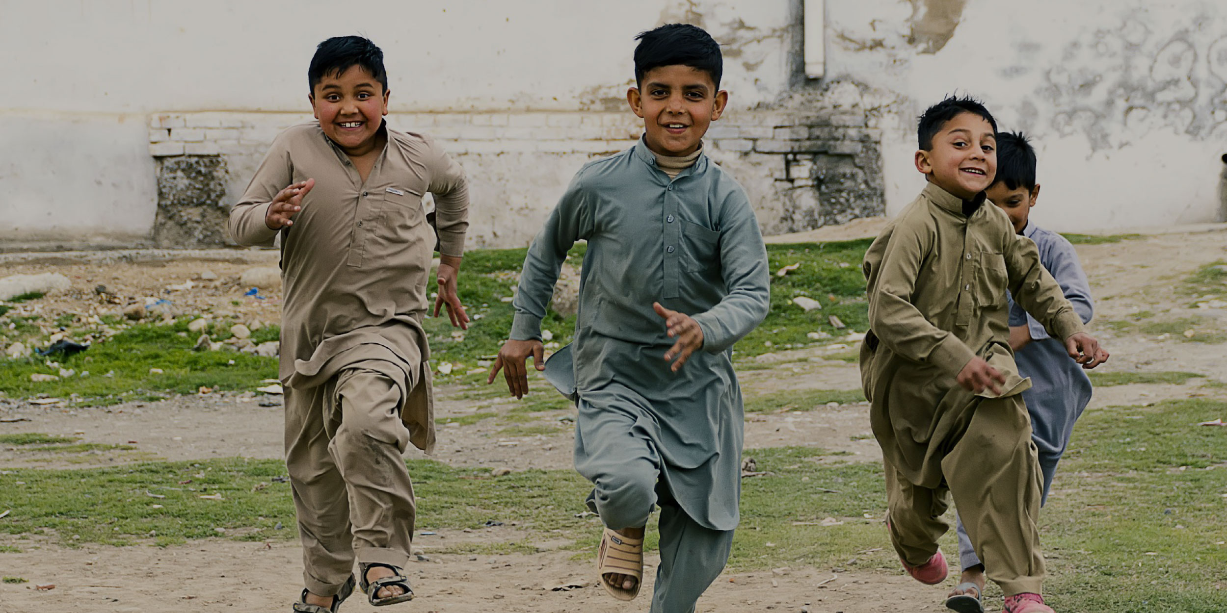 Three Pakistani boys running in traditional clothing