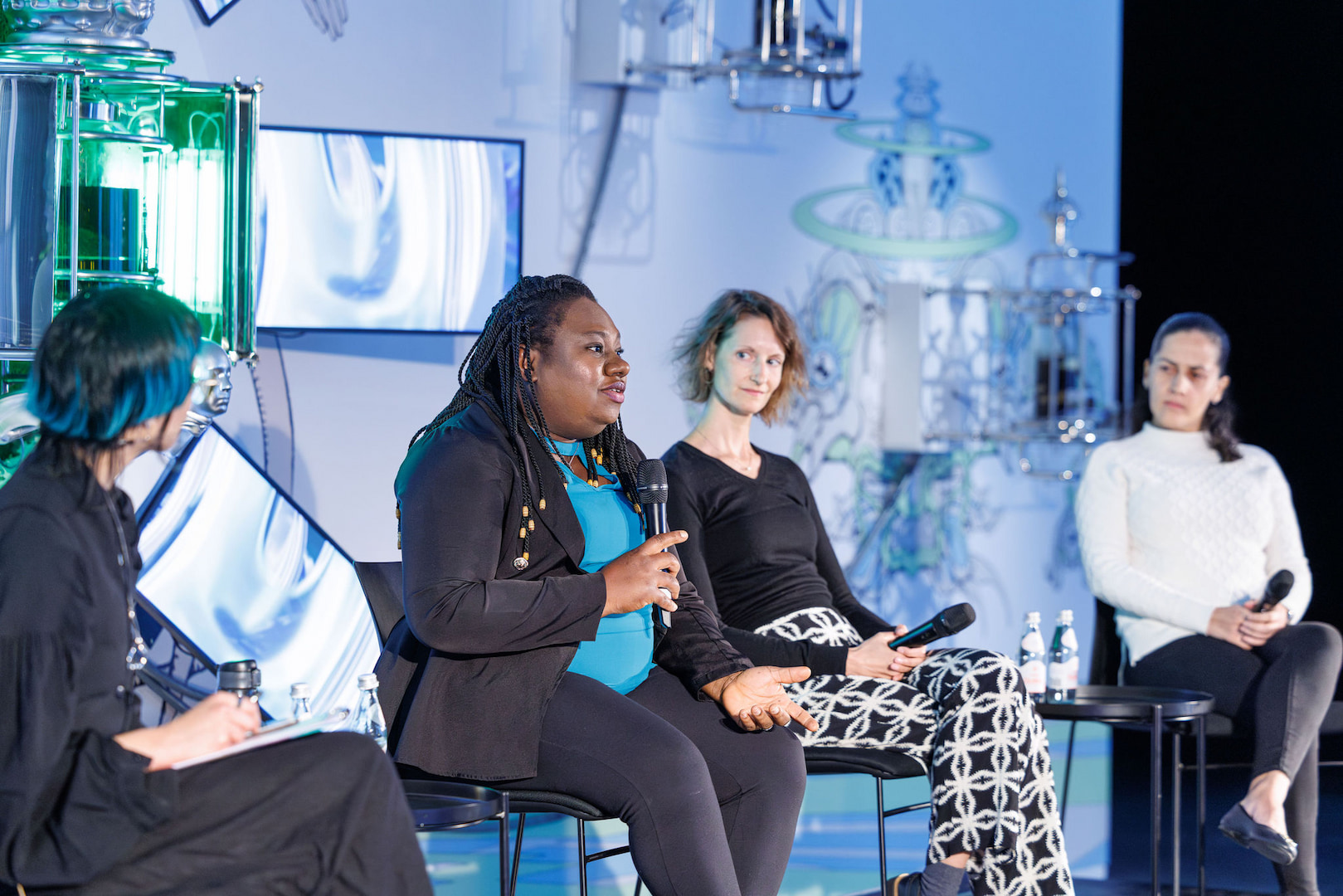four panellists speak at a forum in front of an artwork in a gallery space