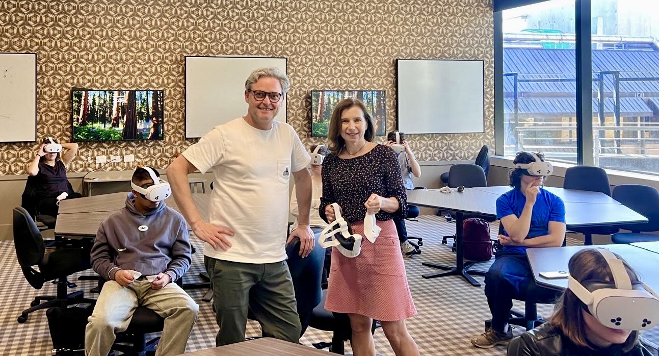Image of Elisabetta Ferrari and Mitch Buzza surrounded by students in a classroom wearing VR headsets. 