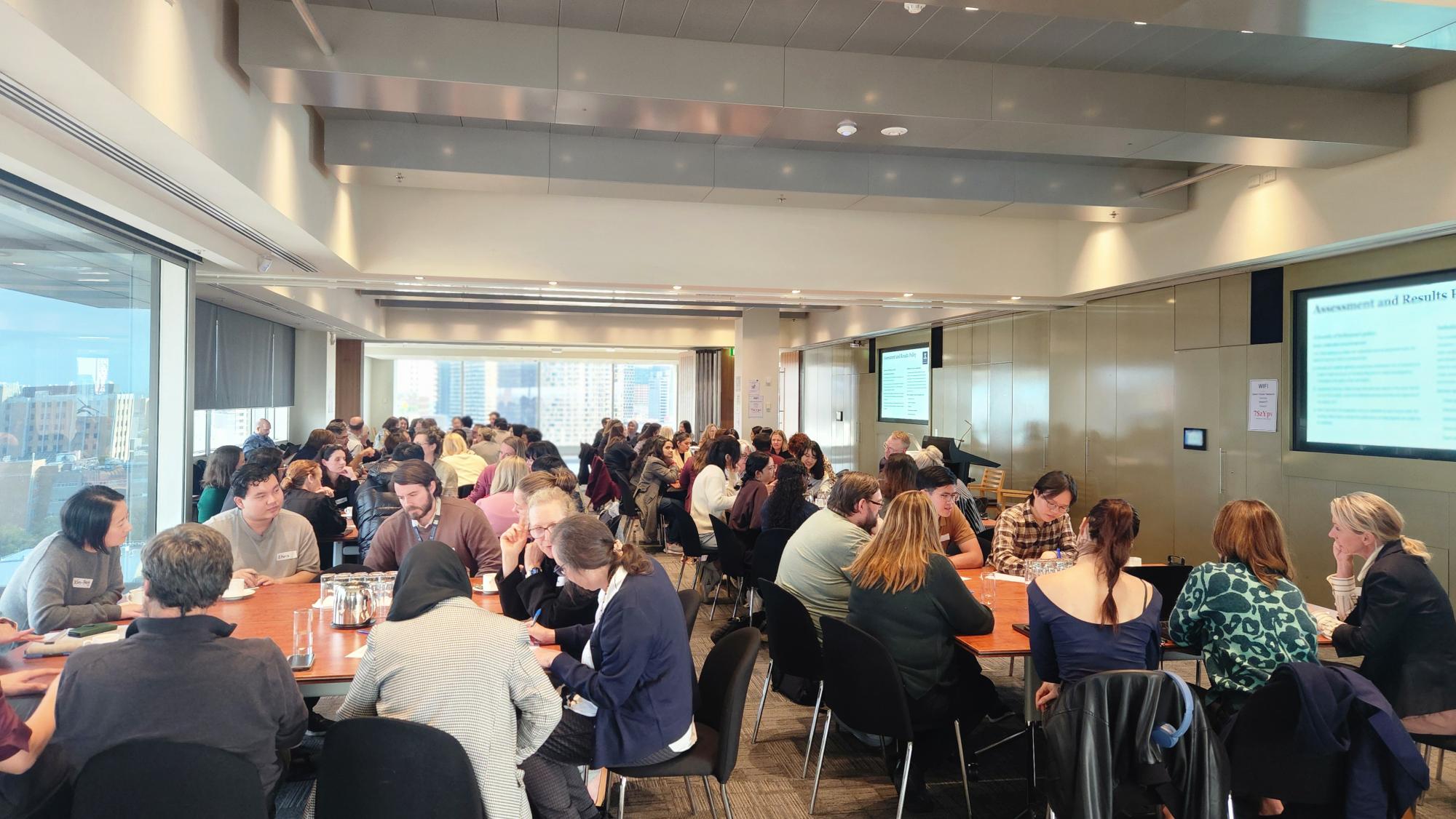 Image of a room full of students and teachers sitting in groups at tables 