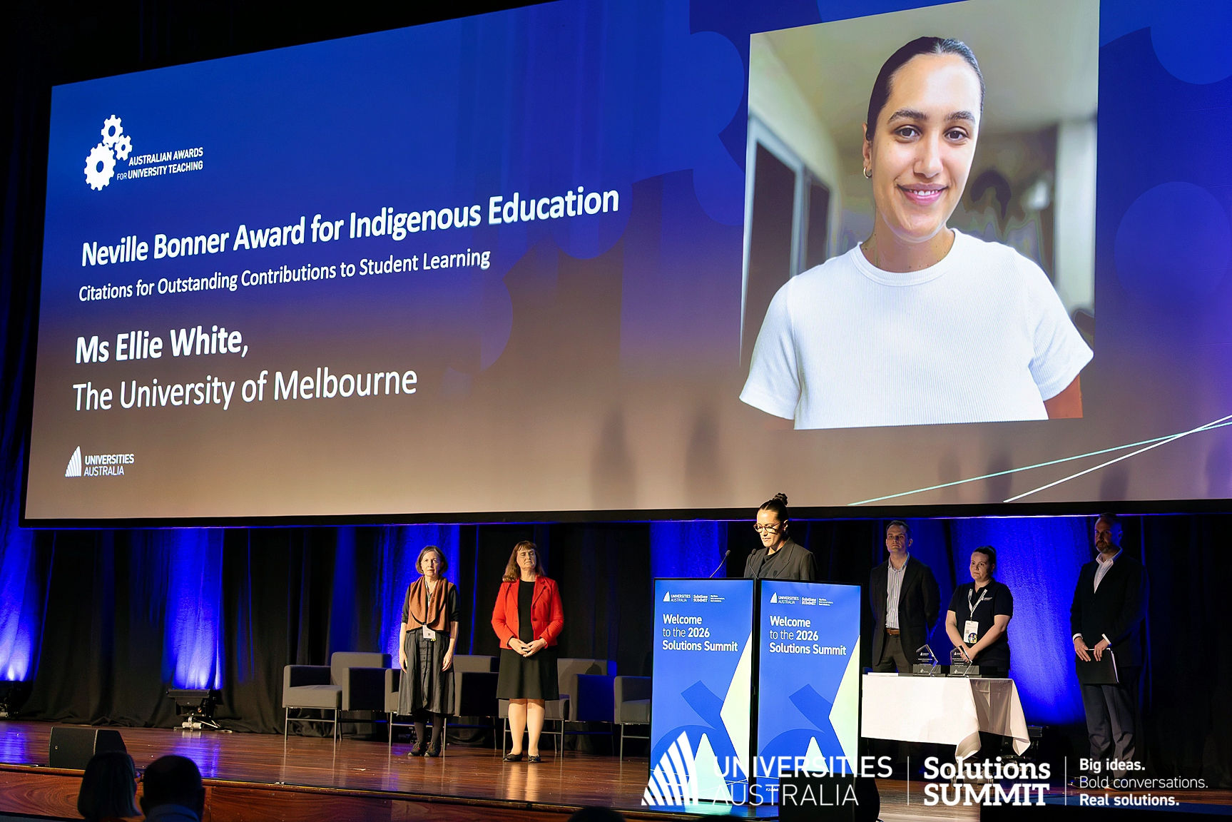 Image of Ms Ellie White on a stage at a podium, presenting at the Universities Australia Summit 